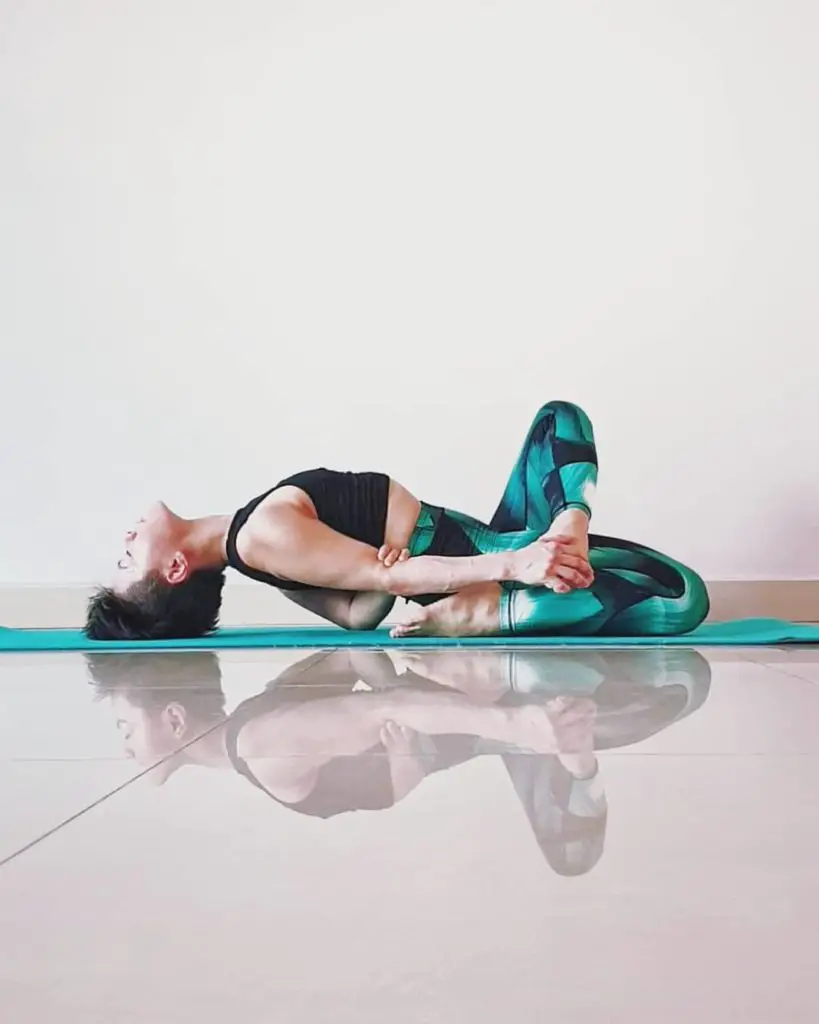 A lady on a green yoga mat performing Matsyasana - yoga for hair growth and glowing skin