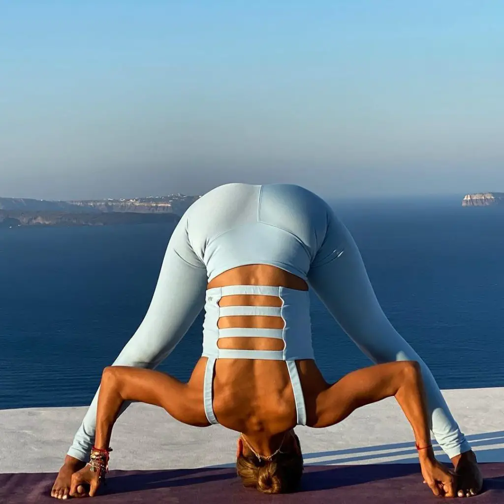 A lady in sky blue outfit performing Prasarita padottanasana at sea side - yoga for hair growth on bald head