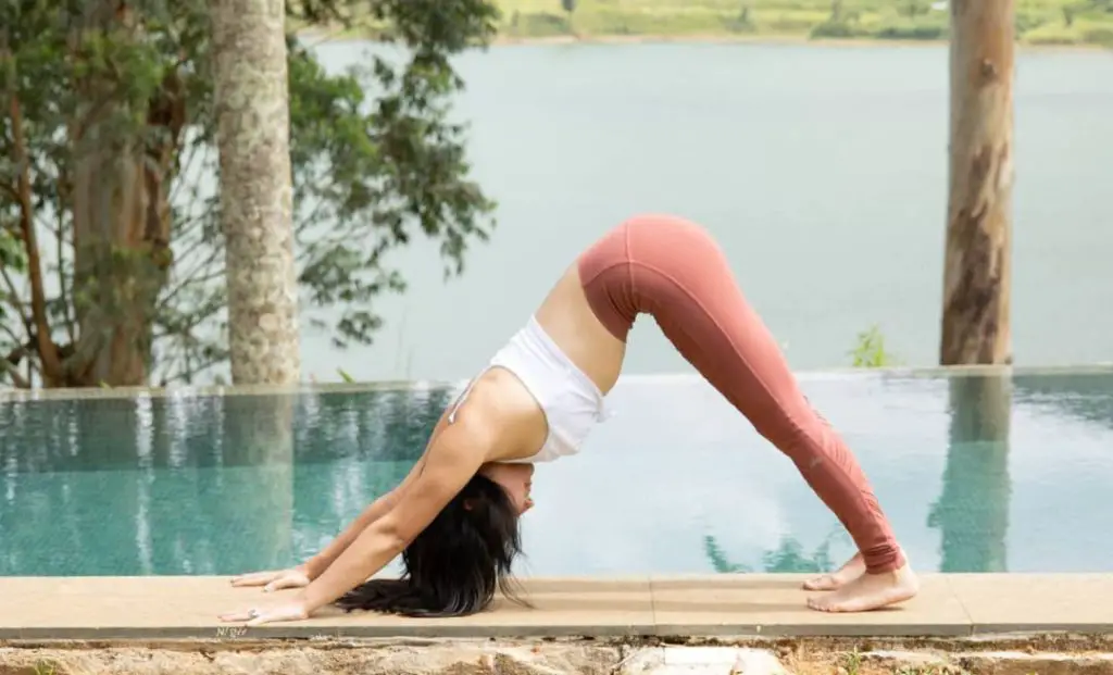 A lady in pink bottom and white top performing Adho Mukha Svanasana at a pool side - yoga for hair fall control and growth