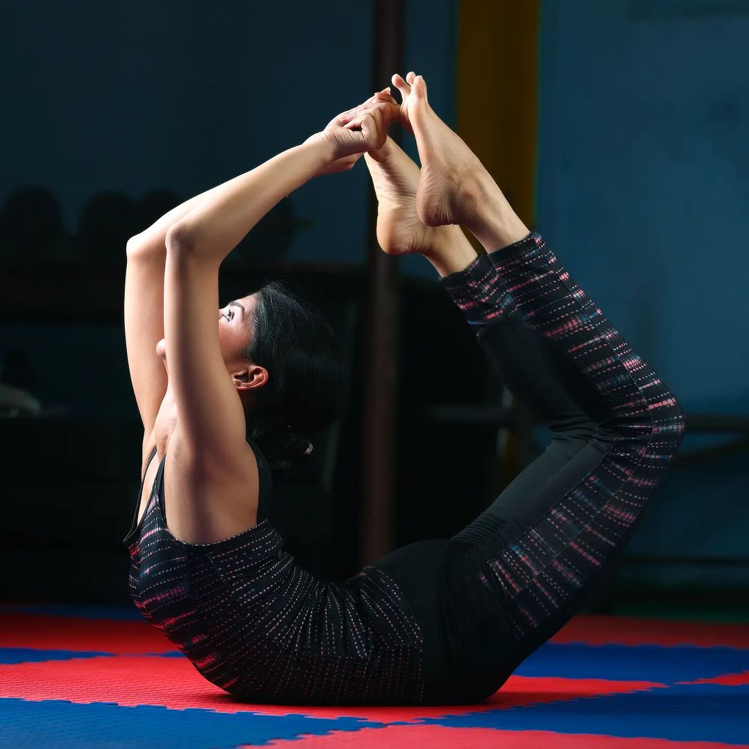A woman in black outfit performing Dhanurasana - yoga asanas to reduce belly fat