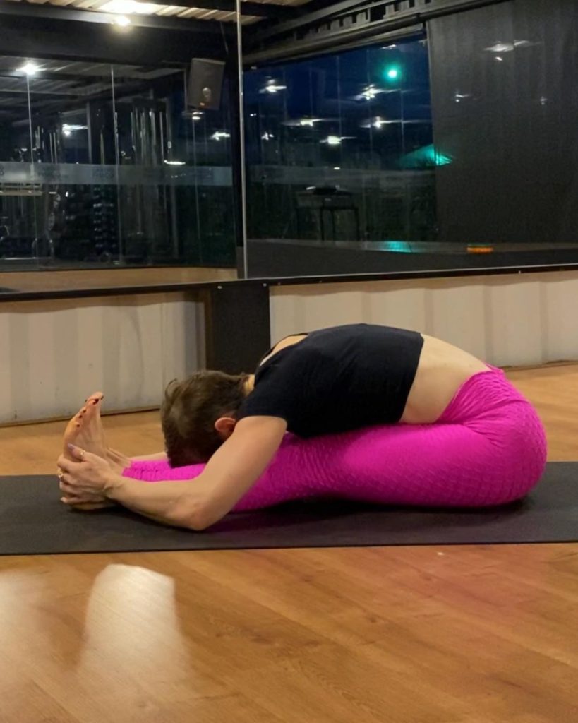 A woman in pink and black outfit is performing Paschimottana - yoga to flat tummy